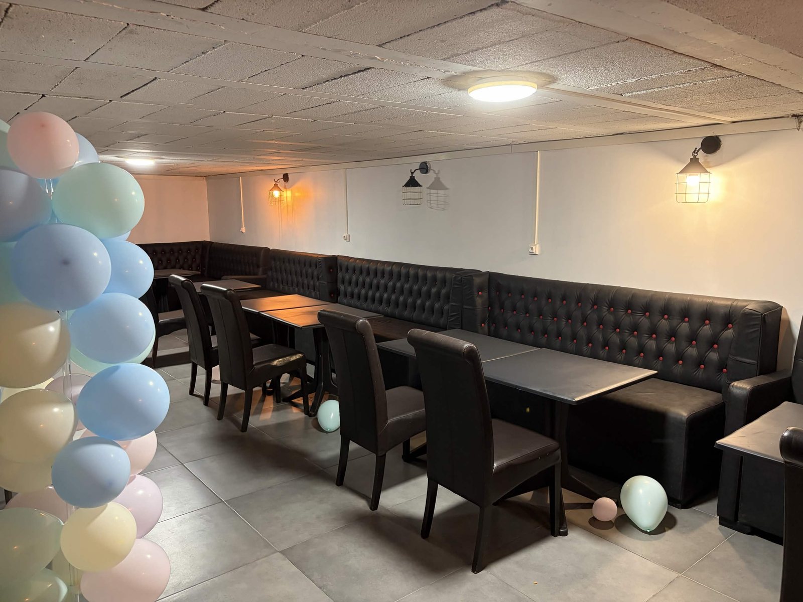 Salle privée du bas avec banquettes chesterfield noir et arche de ballons pastel